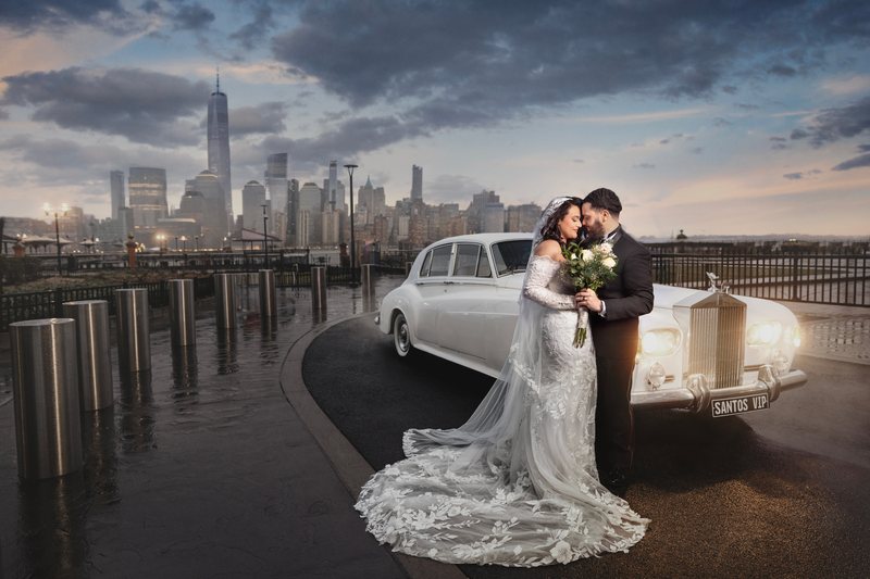 Black and white photograph of a bride being helped from a white classic wedding car at the curb