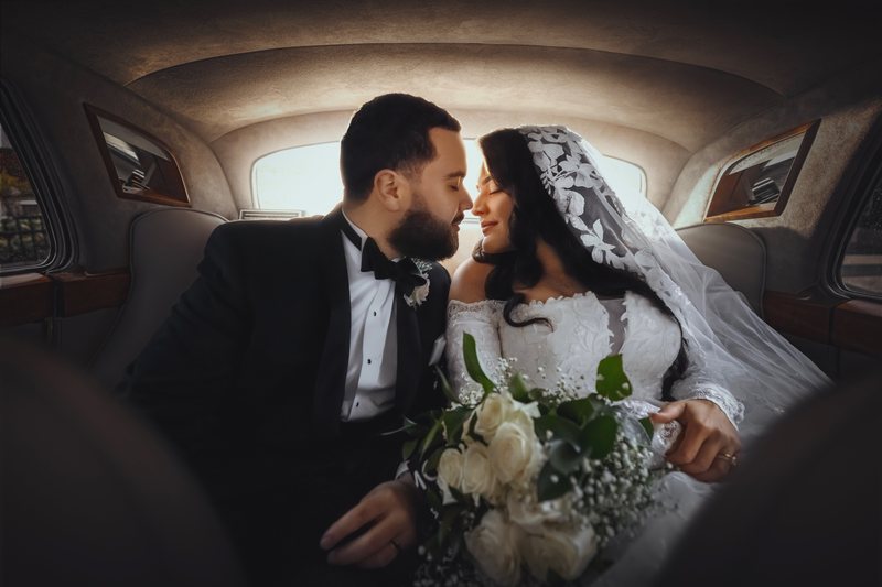 Bride and groom in the back seat of a vintage wedding car, foreheads together, bouquet in her lap