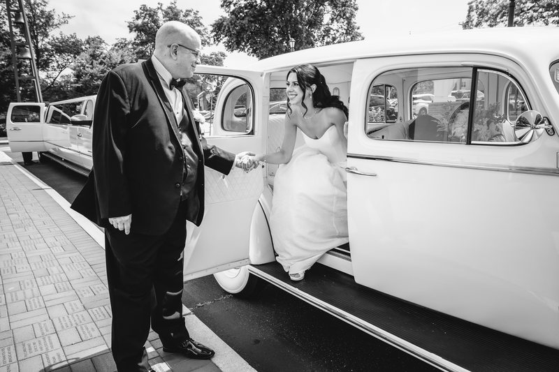 Couple hand in hand beside a white 1930s classic wedding car outside an oceanfront venue