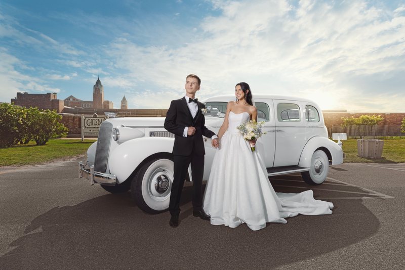 Bride and groom beside a white classic Rolls-Royce at the waterfront with the Manhattan skyline behind them