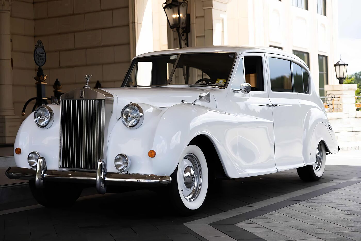 White vintage Rolls-Royce Princess wedding car beneath a porte-coch&egrave;re, chrome grille and whitewall tires detailed for the day