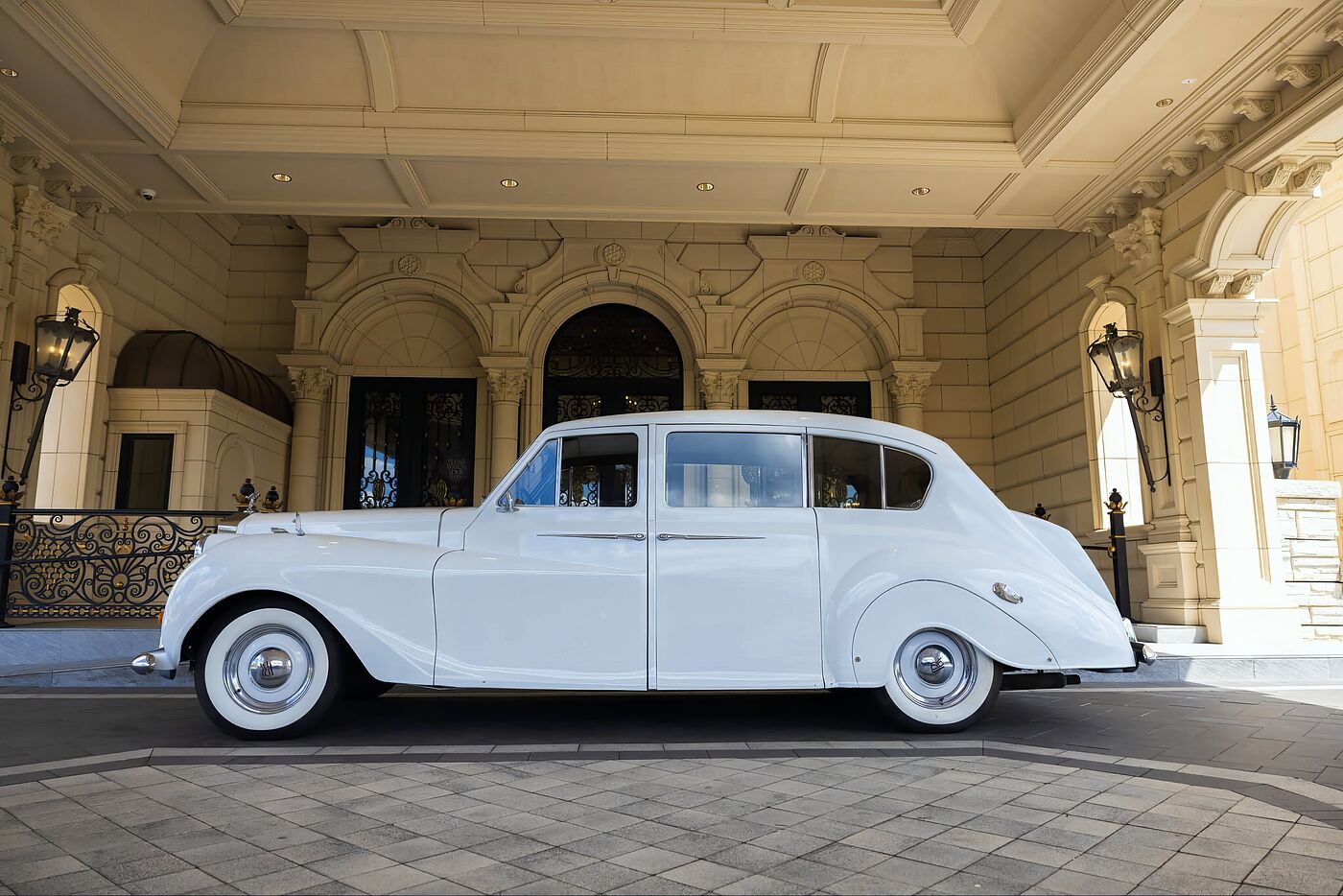 White vintage Rolls-Royce Princess parked beneath the stone portico of a luxury wedding venue