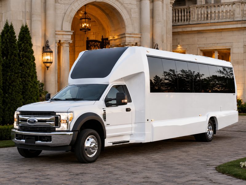 White party bus with tinted windows parked at the arched entrance of a stone estate